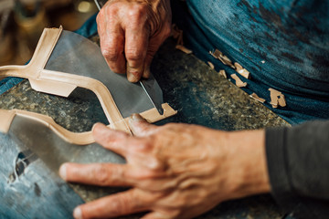 Hands of an old and experienced worker in the handmade shoe industry, performing assembly tasks with a blade, in his work section, refining the leather.