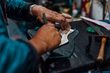 Hands of an old and experienced worker in the handmade shoe industry, performing gluing and sewing tasks, putting glue on a piece of genuine leather.