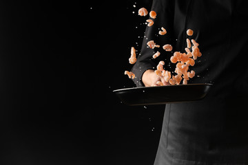Chef cooks seafood, shrimp in a pan. On a black background for design. Freeze in motion.