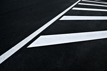 A fragment of white reflective paint road signage on black asphalt road, perspective view.
