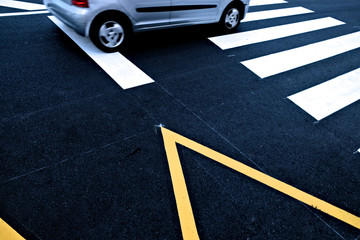 A car on a zebra crossing, road signage on black asphalt road.
