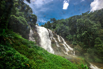 Natural blurred background of waterfalls, fast-flowing currents and water droplets from the wind blowing among the rocks and surrounded by big trees, spontaneous beauty