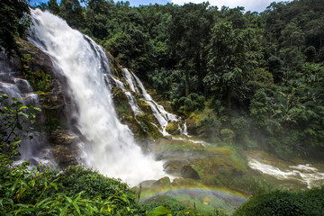 Natural blurred background of waterfalls, fast-flowing currents and water droplets from the wind blowing among the rocks and surrounded by big trees, spontaneous beauty