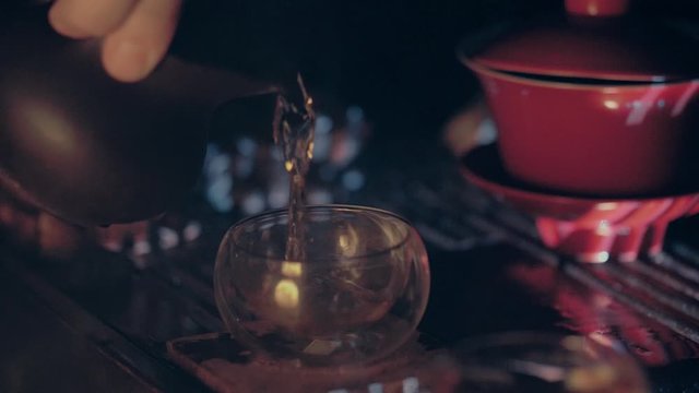 Tea master is pouring tea in the tea cup from the gaiwan and putting it back on the tea board. Tea ceremony, a very important part of Chinese culture.