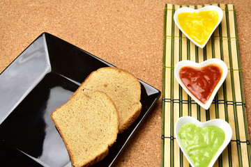 white heart shape bowl with colorful sauces on cork and bamboo mat background