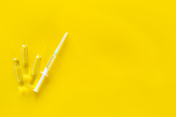 Flu vaccination. Ampoule and syringe on yellow background top view copy space