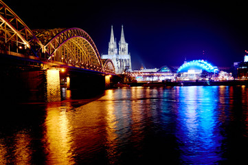 Fototapeta premium Evening view of the illuminated Cologne Cathedral and the bridge over the Rhine from the opposite bank of the river
