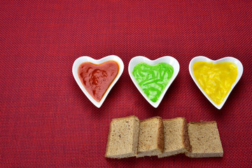 Fototapeta na wymiar white heart shape bowl with sauces with cut breads on red background