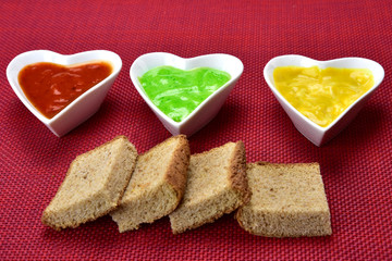 Fototapeta na wymiar white heart shape bowl with sauces with cut breads on red background