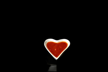 White porcelain heart shape bowl with colorful sauces on black background