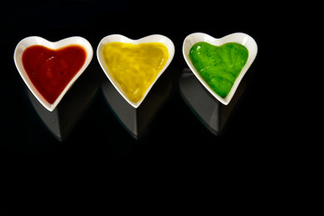 White porcelain heart shape bowl with colorful sauces on black background