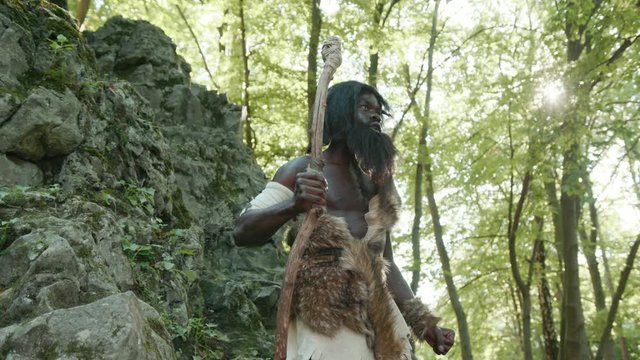 Prehistoric afro tarzan wildman of hunter-gatherers tribe in rocks landscape beating in chest and screaming of pride. Freedom first people. Homo sapiens.