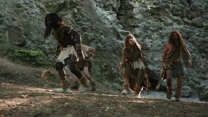 Primitive tribe of wary neanderthals walking slowly in prehistoric forest on hunt or migration. Aboriginal cave people rejoicing with pride and freedom. Homo sapiens.