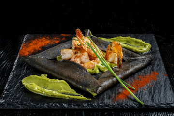Pancakes made of black dough, with shrimp and sauces. Laid out on black slate.