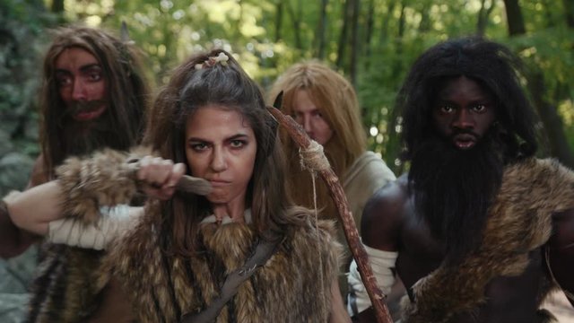 Neanderthal tribe of wild savage people with woman leader growling looking at camera. African primitive family of aboriginal hunter-gatherers in paleolithic period.