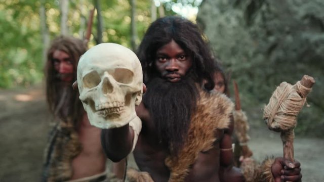Prehistoric wild tribe of neanderthal cannibalists showing human skull close-up. Dangerous cave hunter people. Human cannibalism and wildlife.