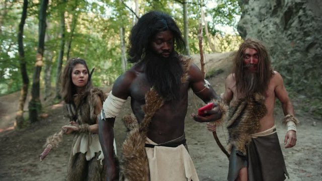 Ancient neanderthals tribe people hunting in forest looking at miracle smartphone rejoicing with future technology growling like gorillas. Multi-ethnic homo sapiens.