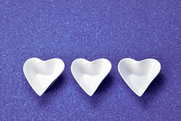 White porcelain heart shape bowl with colorful sauces on blue background.