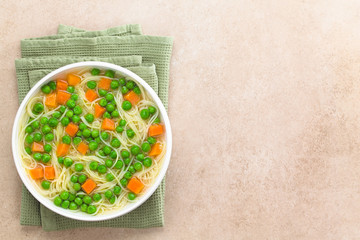 Fresh homemade vegetable noodle soup with carrot, peas, onion and angel hair pasta in white soup bowl, photographed overhead with copy space on the right side (Selective Focus, Focus on the soup)