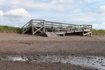 Wooden Ramp on Empty Beach with Cloudy Blue Sky and Rocky Sand