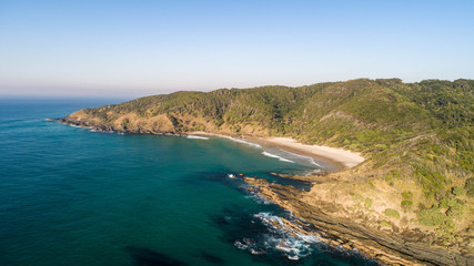Aerial of a spectacular coastal scene with beach, ocean and cliffs on the side of a tropical forest for a beautiful holiday destination.