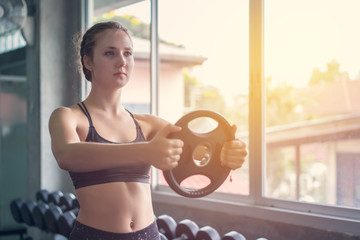 Young woman weightlifter lifting bench press working out with dumbbell in the gym