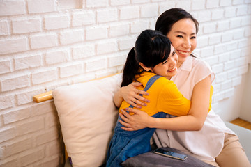 Loving smiling Asian women hugging happily while sitting together on couch at living room