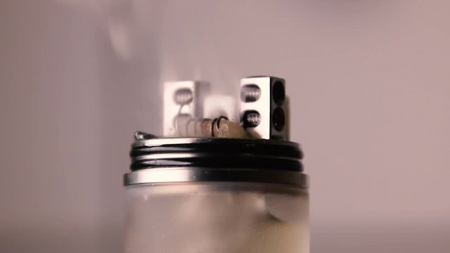Smoke coming out of the wet wadding on vape coil. Coil heating of RDA atomizer for vaping or e-cigarette.
