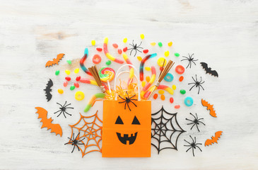 holidays image of Halloween. paper gift bag, spider, bats and sweets over wooden white table. top view, flat lay