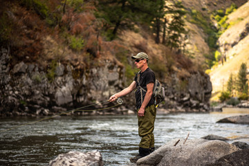 Fly fisherman casting in the mountain stream during the fall season.