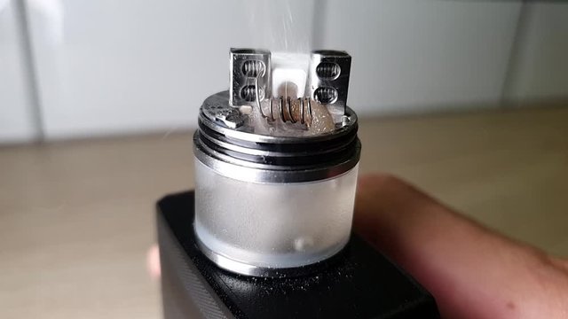 Macro footage of new clapton coil mounted in the electronic cigarette. Smoke coming out of the wet wadding on vape coil.