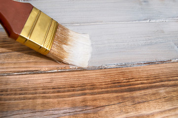painting brush covers the wood textured floor with white paint close up side view from above