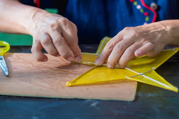 Eldery woman making and build star-shaped kite or thai name Chula kite for sale at local market. Selective focus on .left hand finger..
