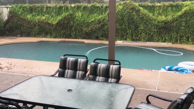 Hard driving rain bounces off the pool water and glass tabletop of a poolside table, Scottsdale, Arizona.