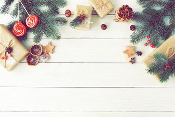 Christmas background with fir twigs, gifts, red berries, cones, sinnamon sticks and Xmas decor on white wooden background top view. Copy space