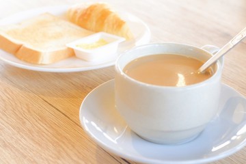 Fresh delicious breakfast with hot coffee in white cup and blur crispy toasts on wooden table.