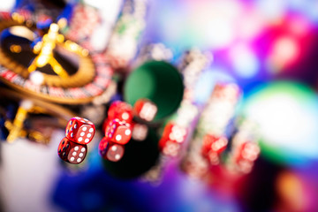 Casino - gambling games. Roulette wheel, dice and stack of poker chips on colorful bokeh background.