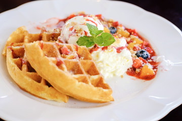 Sweet waffles with strawberries sauce vanilla ice cream fresh fruit and mint leaf on white plate at cafe restaurant in holiday summertime.