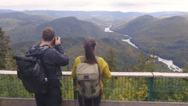 Hiking couple with backpacks in Quebec National Park in Autumn season taking photos in Canada forest travel lifestyle. Tourists looking at view of Jacques Cartier National Park.