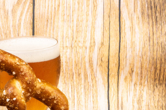 Ressource graphique avec espace négatif pour texte pour la fête de la bière (oktober fest) avec un fond bois clair et un verre de bière et un bretzel géant en angle