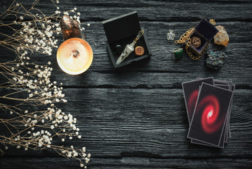 Tarot cards, dried flowers, burning candle and magic potion vial on a black wooden table background.