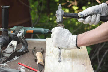 Carpenter is working by a chisel and hammer with a wooden board on his workbench.
