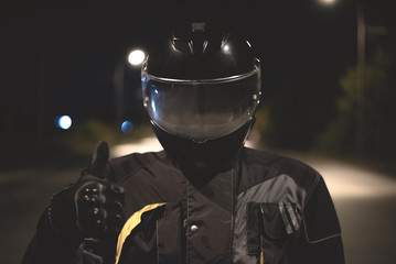 Motorbiker is showing a thumbs up over night road background.