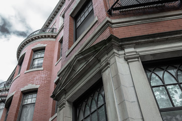 Red brick, gray stone, and wrought iron details on the exterior of an old brownstone apartment building, horizontal aspect
