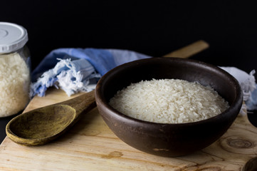 Uncooked rice in clay bowl on a wooden table with black background.