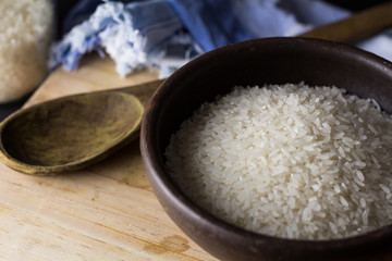 Uncooked rice in clay bowl on a wooden table with black background.