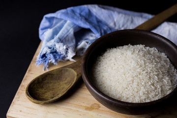 Uncooked rice in clay bowl on a wooden table with black background.