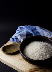 Uncooked rice in clay bowl on a wooden table with black background.