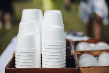Stacks of white plastic containers of red soup or borsch prepared for takeaway service on table with green tablecloth.