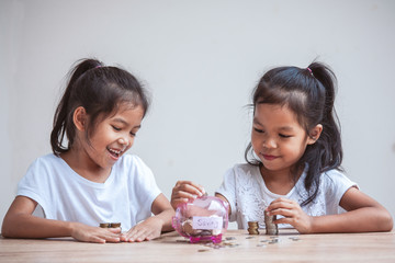 Two cute asian child girls putting money into piggy bank to save money for the future together with fun and happiness